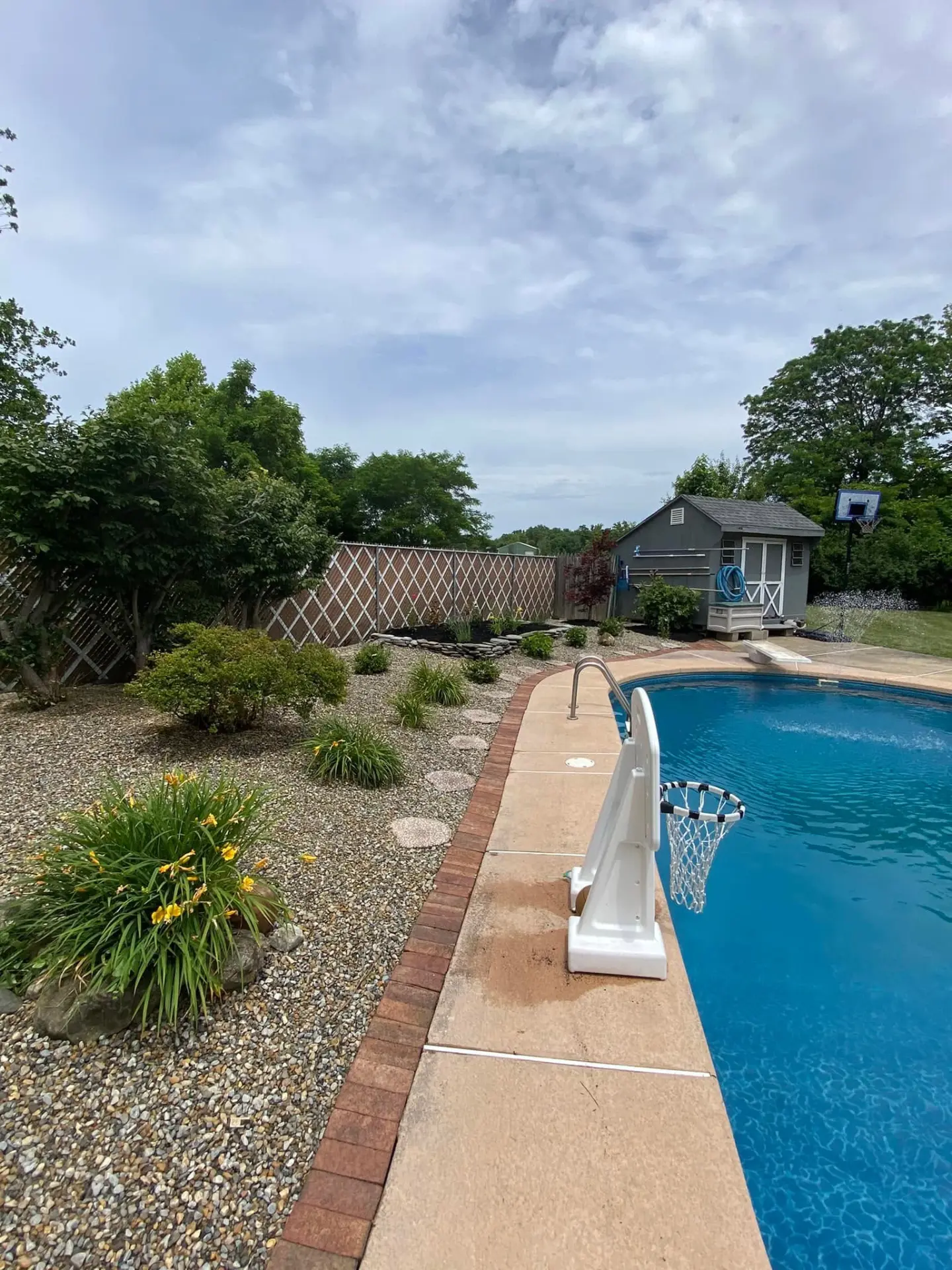 Landscaped stone bed with shrubs and flowers around an in-ground pool