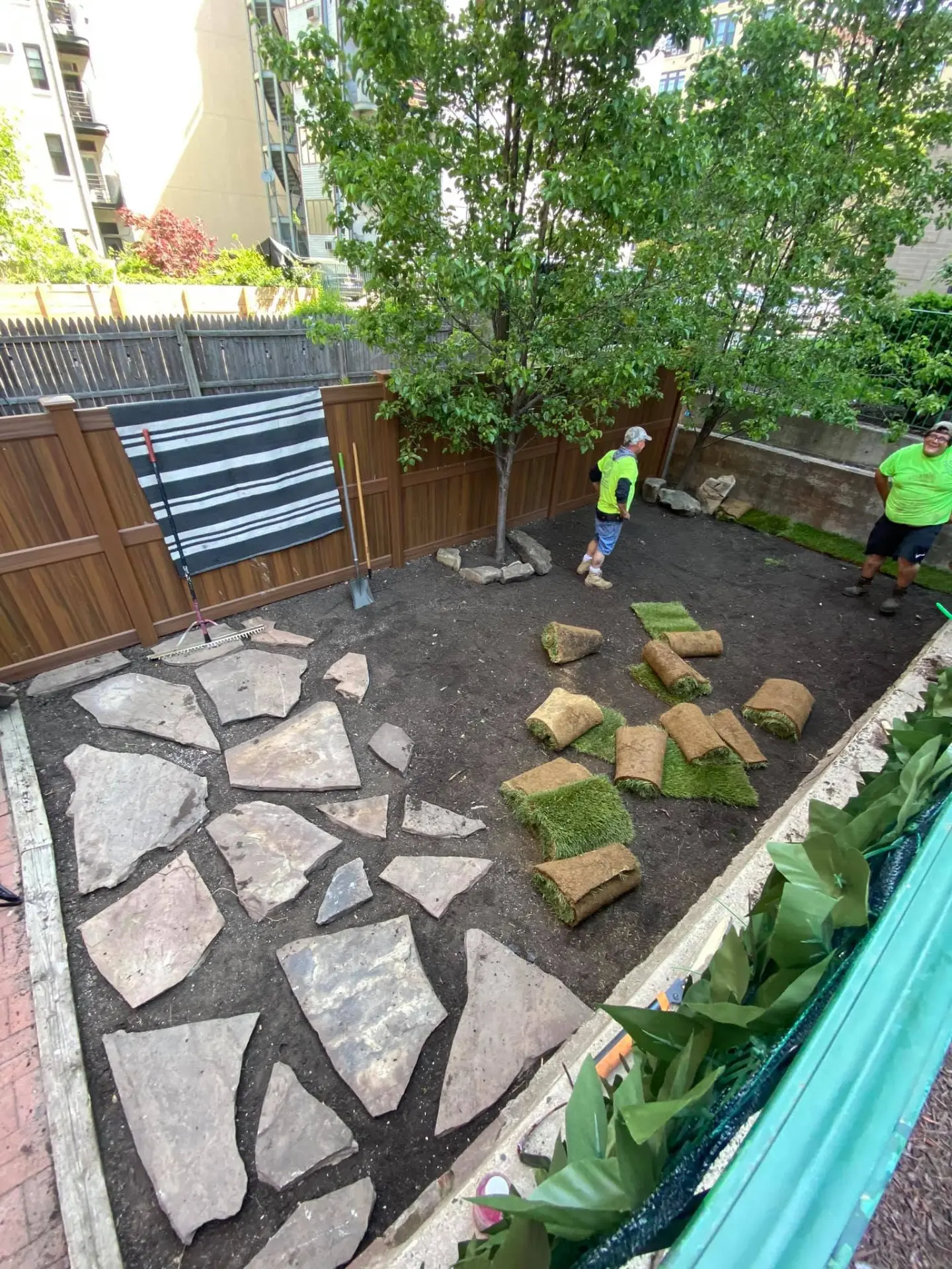 Crew setting flagstone pavers and laying sod in a city backyard