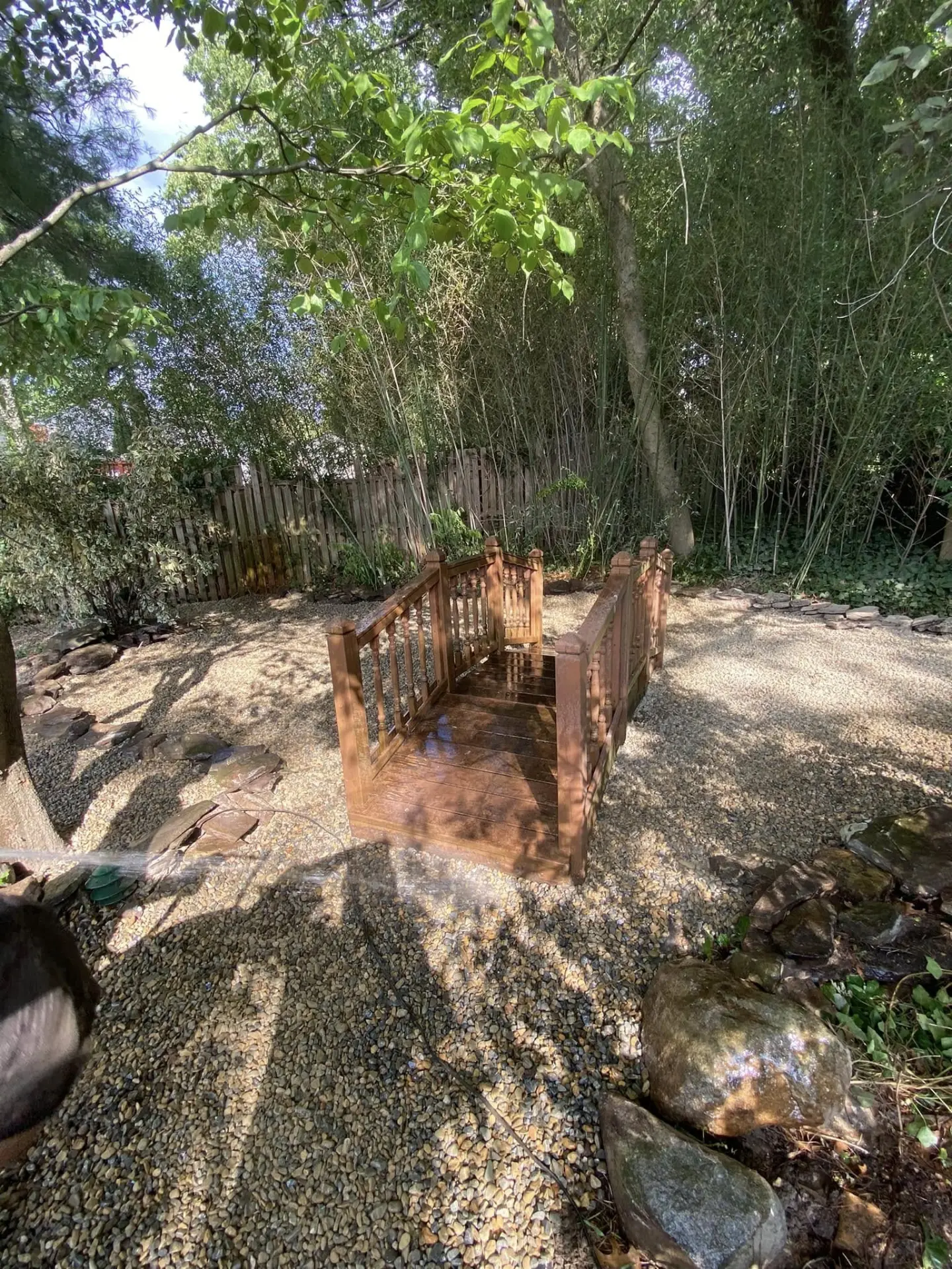 Wooden garden bridge over a stone bed in a shaded backyard